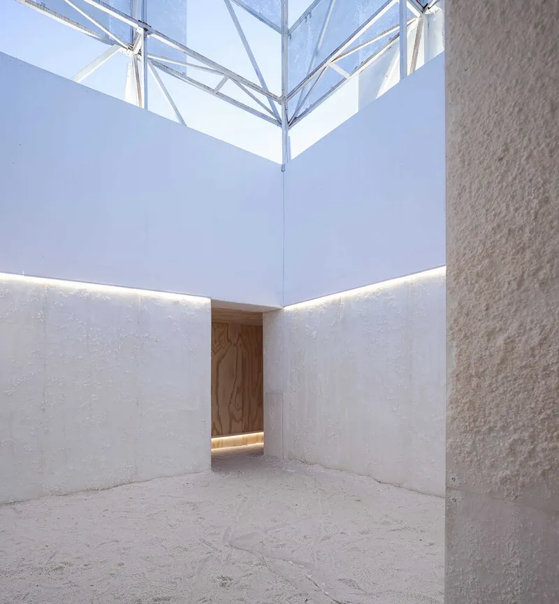 Interior courtyard with white plastered walls and timber doorway under an exposed steel truss skylight