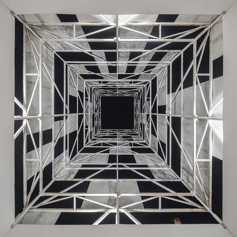 Upward view through the scaffolding tower at night showing illuminated concrete and black void panels