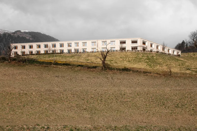 Long white facade with rhythmic window openings set on a grassy slope under an overcast sky