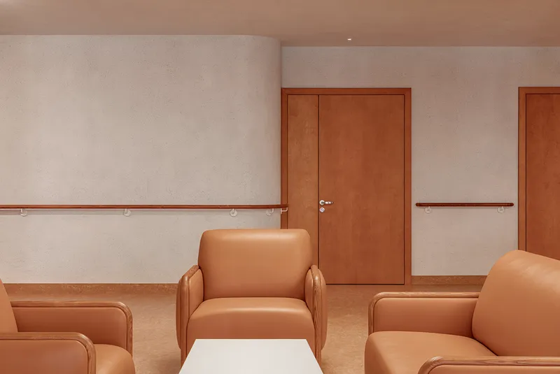 Corridor with tan upholstered armchairs, timber handrails, and wood doors along a white wall