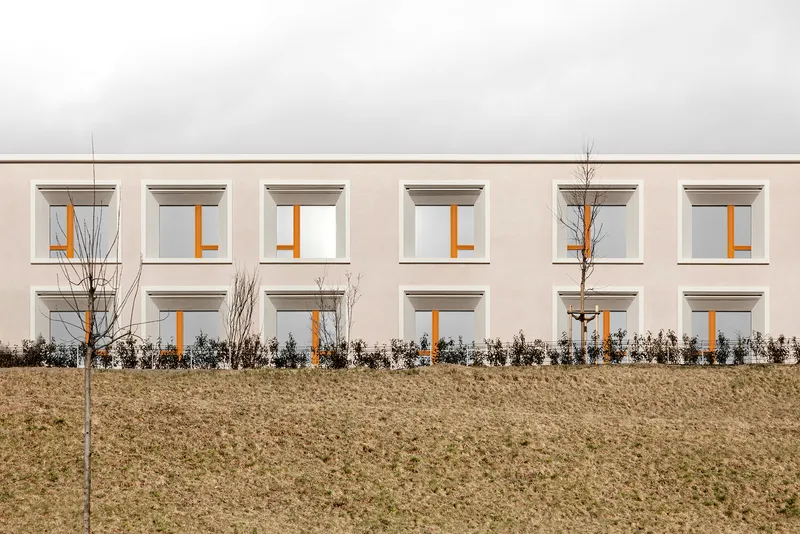 Facade detail showing square windows with deep reveals and timber frames above a planted hedge row