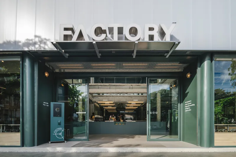 Street view of the glass entrance with teal steel frames beneath a metal canopy and signage above