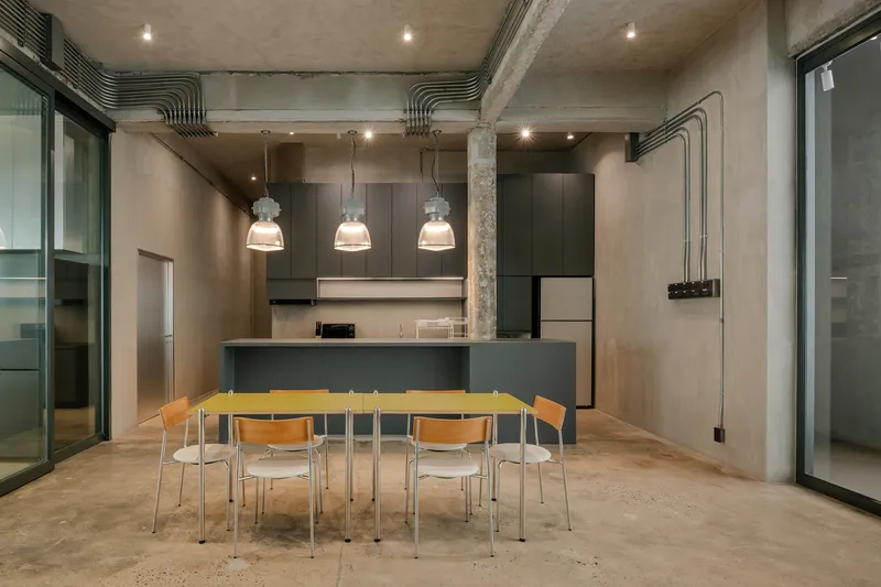 Open kitchen and dining area with exposed concrete columns and pendant lights above yellow table