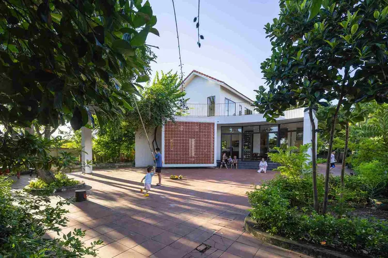 Terracotta tile courtyard with perforated brick screen and children playing beneath mature trees