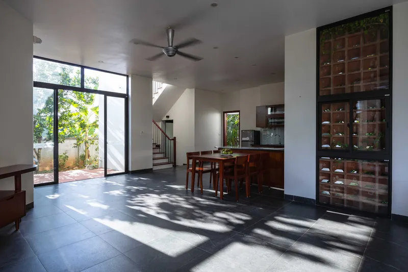 Open living and dining area with dark tile floor receiving dappled sunlight through glazed courtyard door