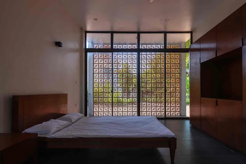 Bedroom with platform bed facing floor-to-ceiling perforated brick screen filtering daylight and garden views