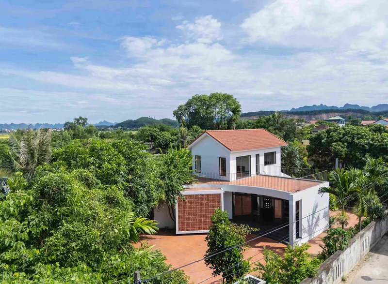 Two-storey white volumes with terracotta tile roofs and perforated brick screen among hills and vegetation