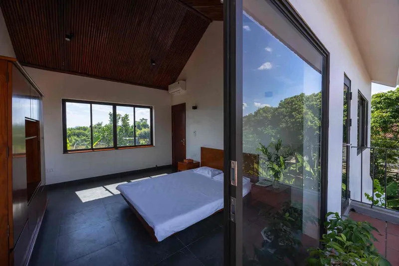 Bedroom with timber slatted ceiling and glass doors opening to a planted terrace under blue skies