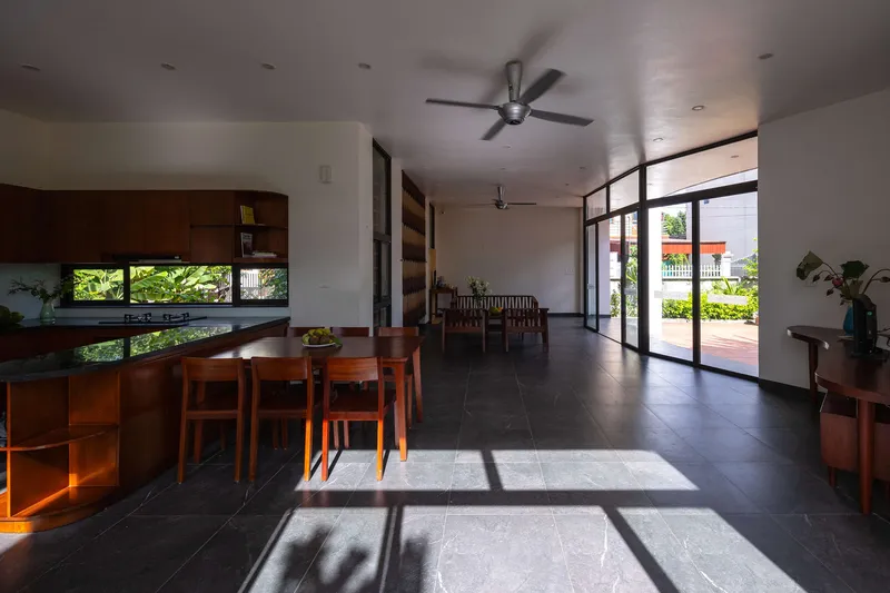 Open-plan dining and living space with dark tile flooring and sunlight streaming through full-height glass doors
