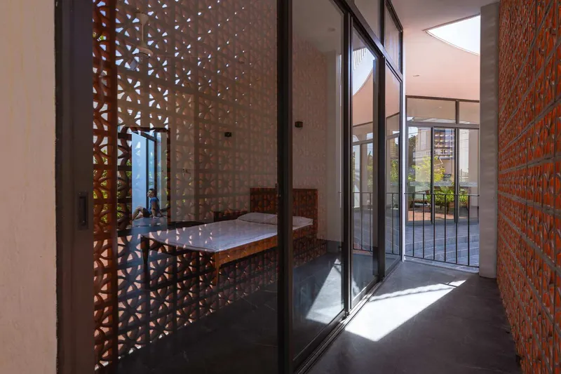 Glazed corridor with perforated terracotta brick screens on either side filtering sunlight onto dark tile floors