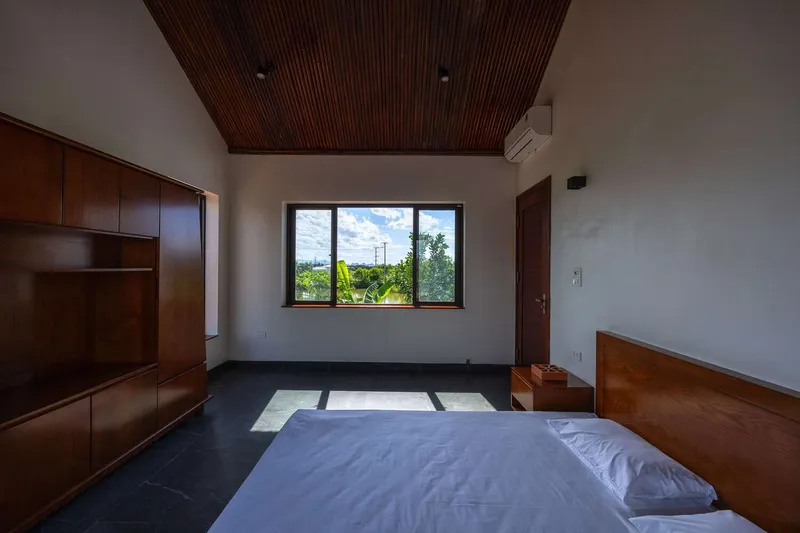 Bedroom with timber ceiling panels and built-in cabinetry framing a window overlooking greenery