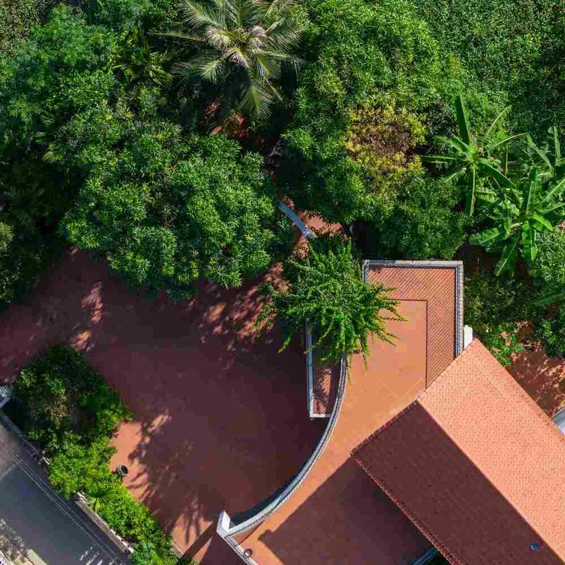 Drone view of terracotta tiled roofs surrounded by dense tropical vegetation and palm trees