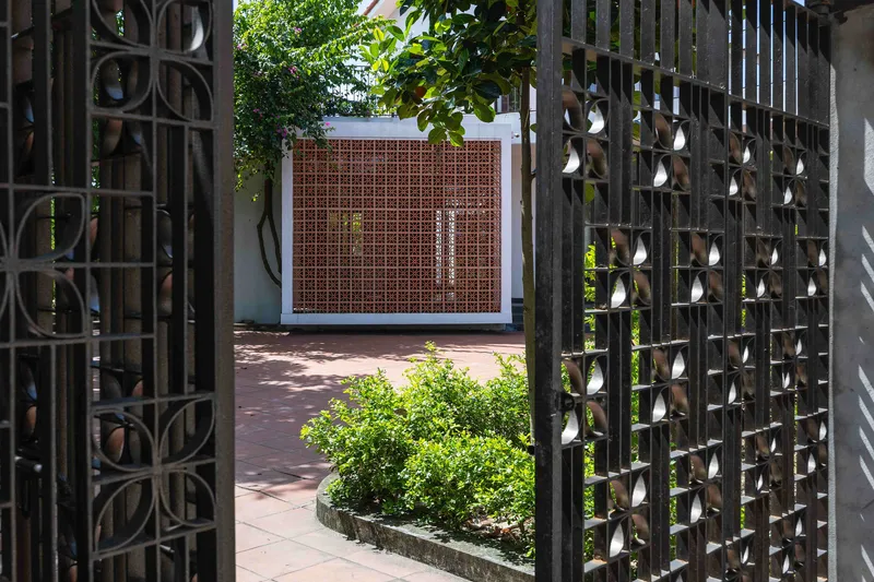 View through decorative perforated concrete screens to a terracotta tile gate panel with planted bed