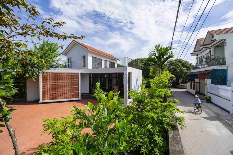 Street view of the white stucco house with perforated brick screen and terracotta courtyard beneath a blue sky