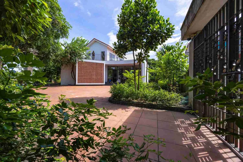 Courtyard with red tile paving, planted beds, and decorative concrete screen under bright sky
