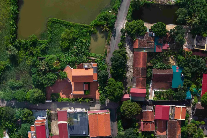 Aerial view of the orange-tiled rooftops and courtyards surrounded by dense tropical vegetation and a pond