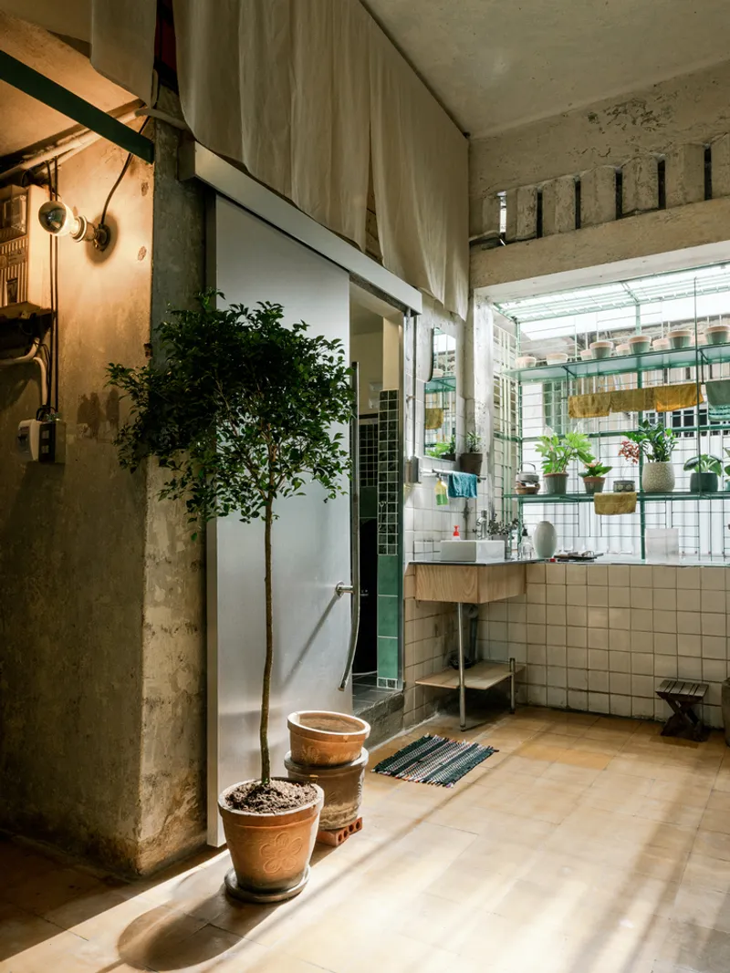 Transition space with white square tile wall, potted tree, and view into adjacent room through steel-framed opening