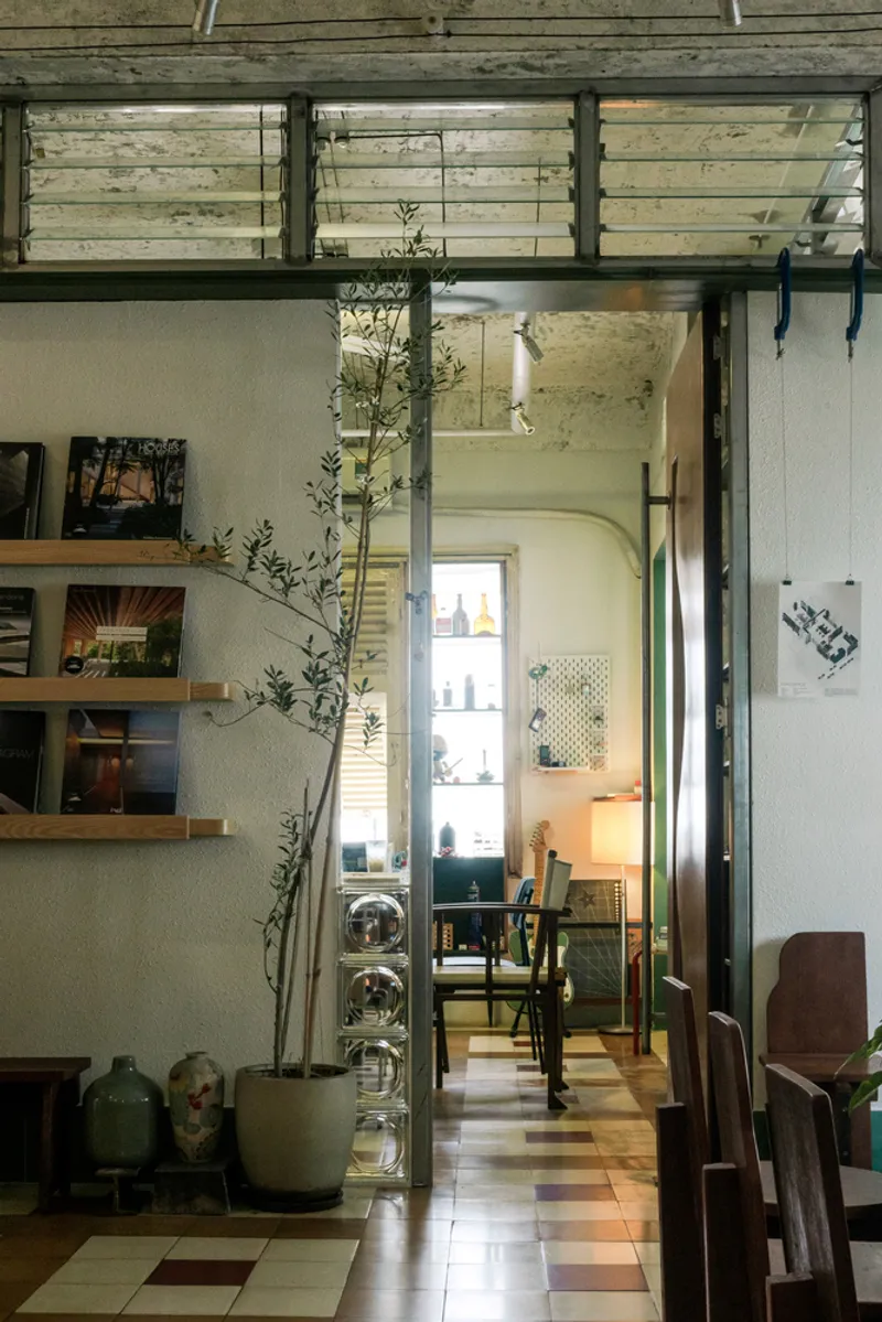 View through steel-framed opening showing checkered floor tiles and slender potted tree in afternoon light