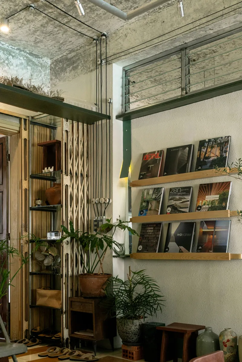 Timber magazine shelves and bamboo room divider beneath a concrete ceiling with hanging plants