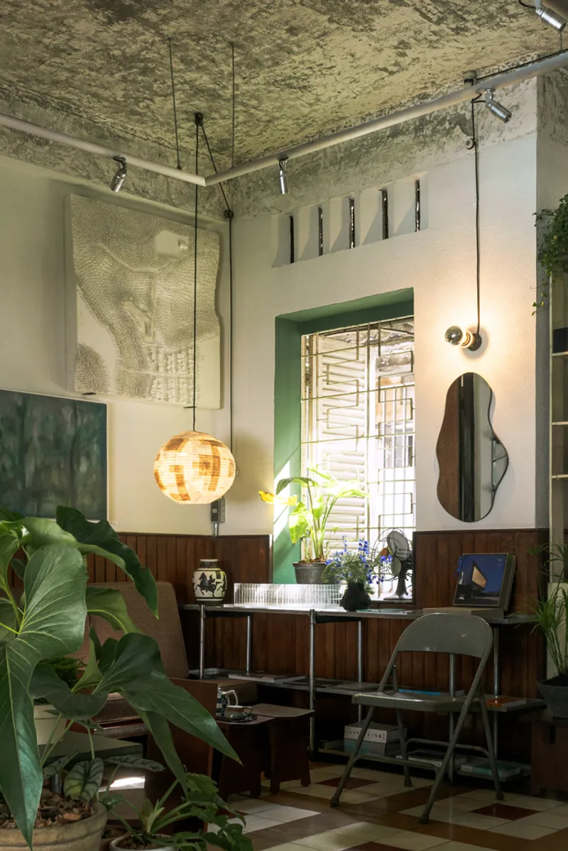 Living area with wood paneling, green door frame and organic-shaped mirror under exposed concrete