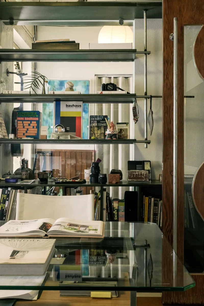 Close-up of glass shelving unit with books and objects suspended by steel rods