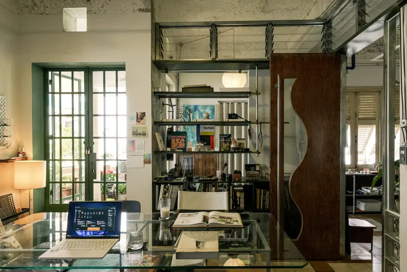 Double-height workspace with exposed concrete ceiling, steel mezzanine and dark timber sliding door