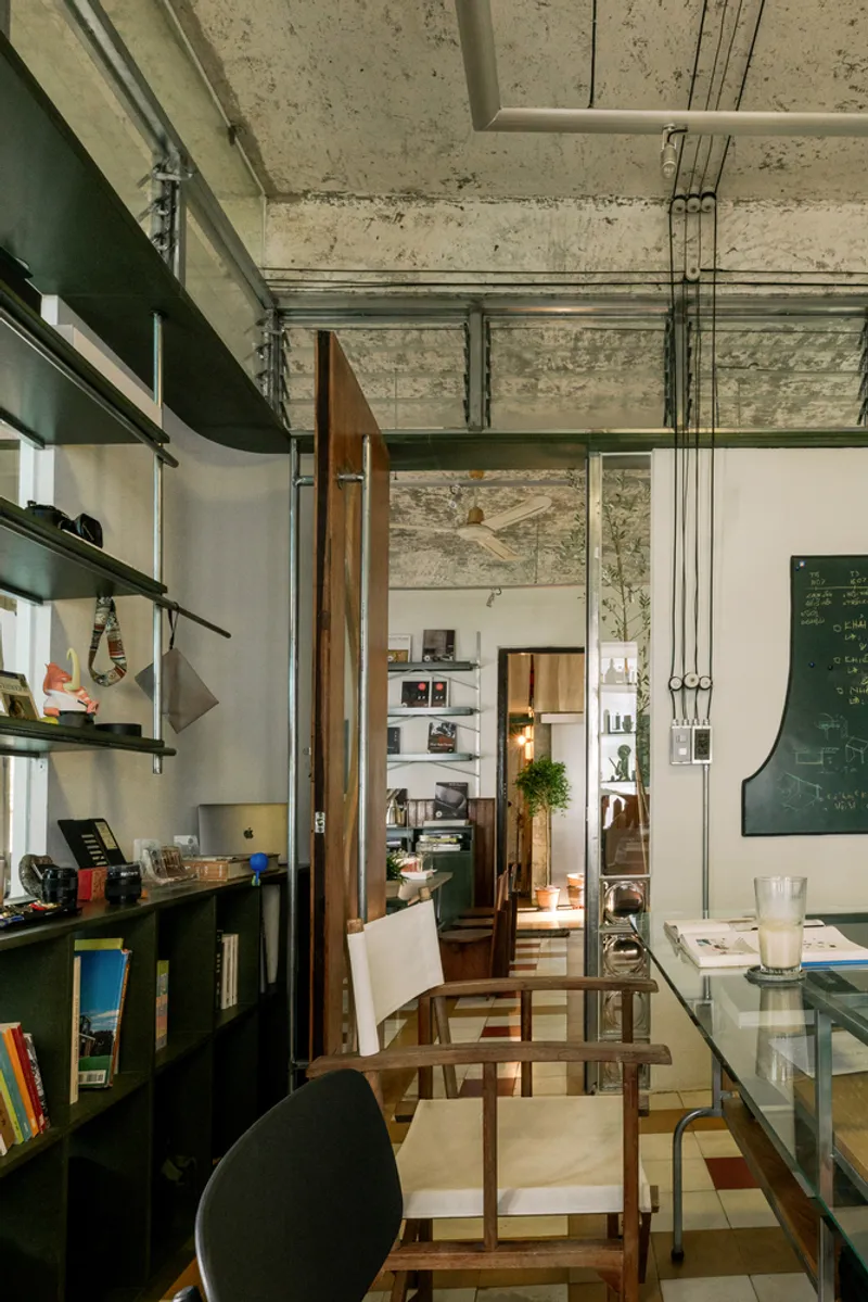 Exposed concrete ceiling with visible conduits above timber-framed doorway and glass-topped table in narrow corridor