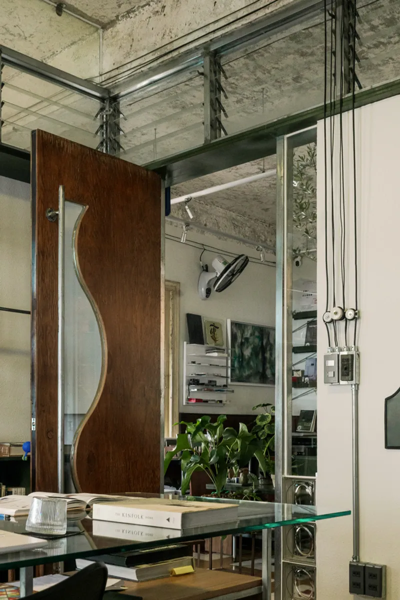 Sculptural timber sliding door suspended from exposed steel tracks beneath a concrete ceiling