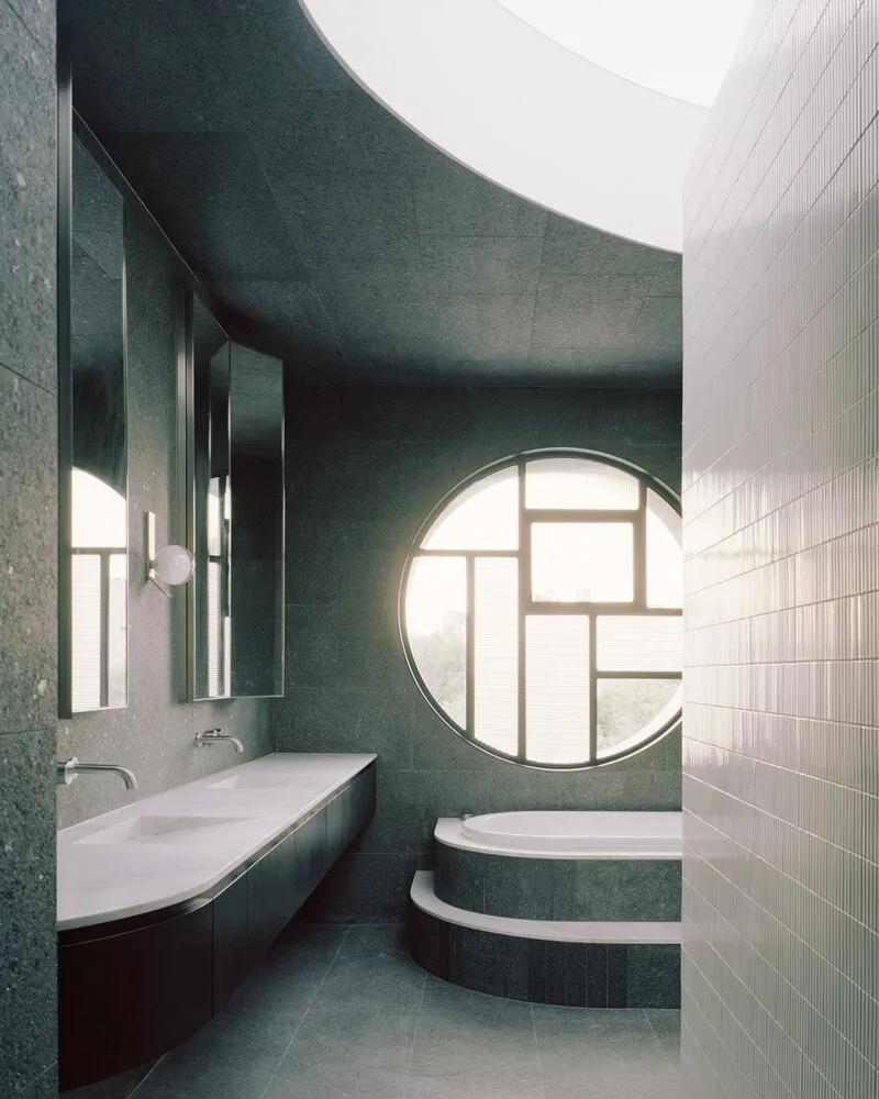 Bathroom with green terrazzo walls, circular window and stepped tub under a curved ceiling