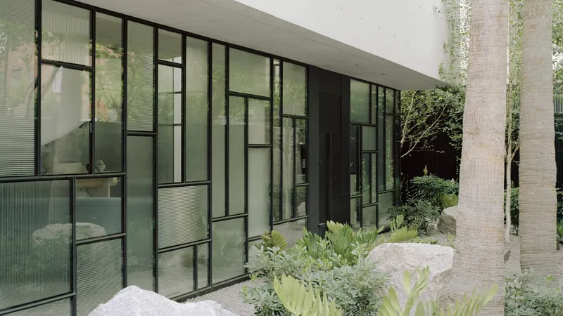 Exterior facade with irregular grid of steel-framed glazing and planted beds with rocks