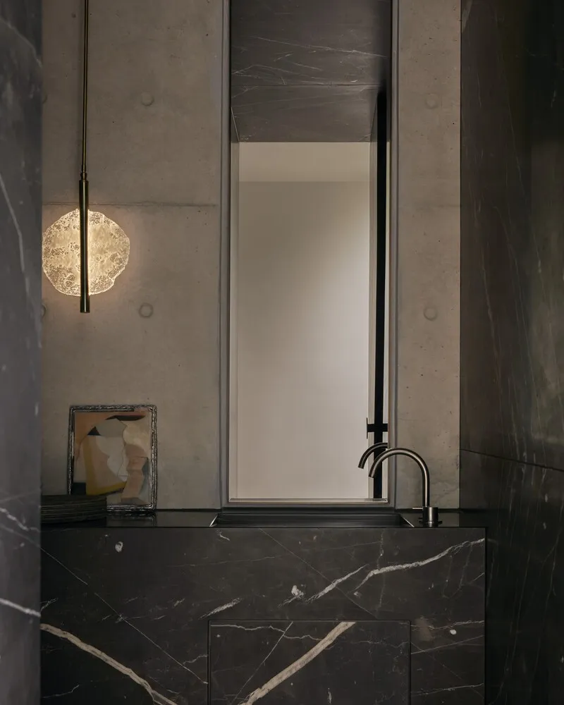 Black marble vanity with integrated basin and tall mirror flanked by cast concrete walls