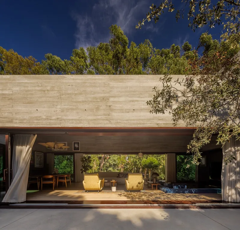 Boarded concrete wall above the fully opened living pavilion with tree shadows on the terrace