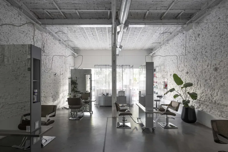 Interior of a salon with exposed white brick walls, timber beamed ceiling and grey styling stations in soft daylight