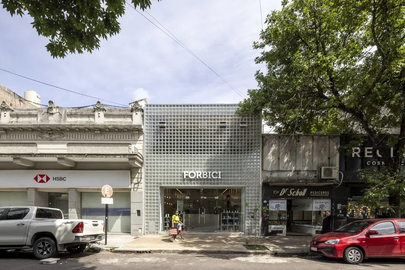 Street facade with white glass block grid wall framing the entrance between neighboring shopfronts under overcast skies