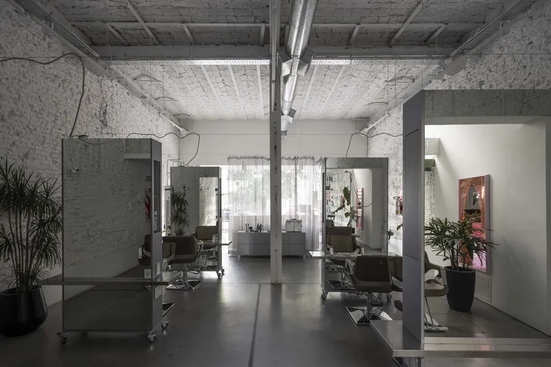 View through the salon showing grey workstation partitions beneath painted brick walls and exposed timber ceiling beams