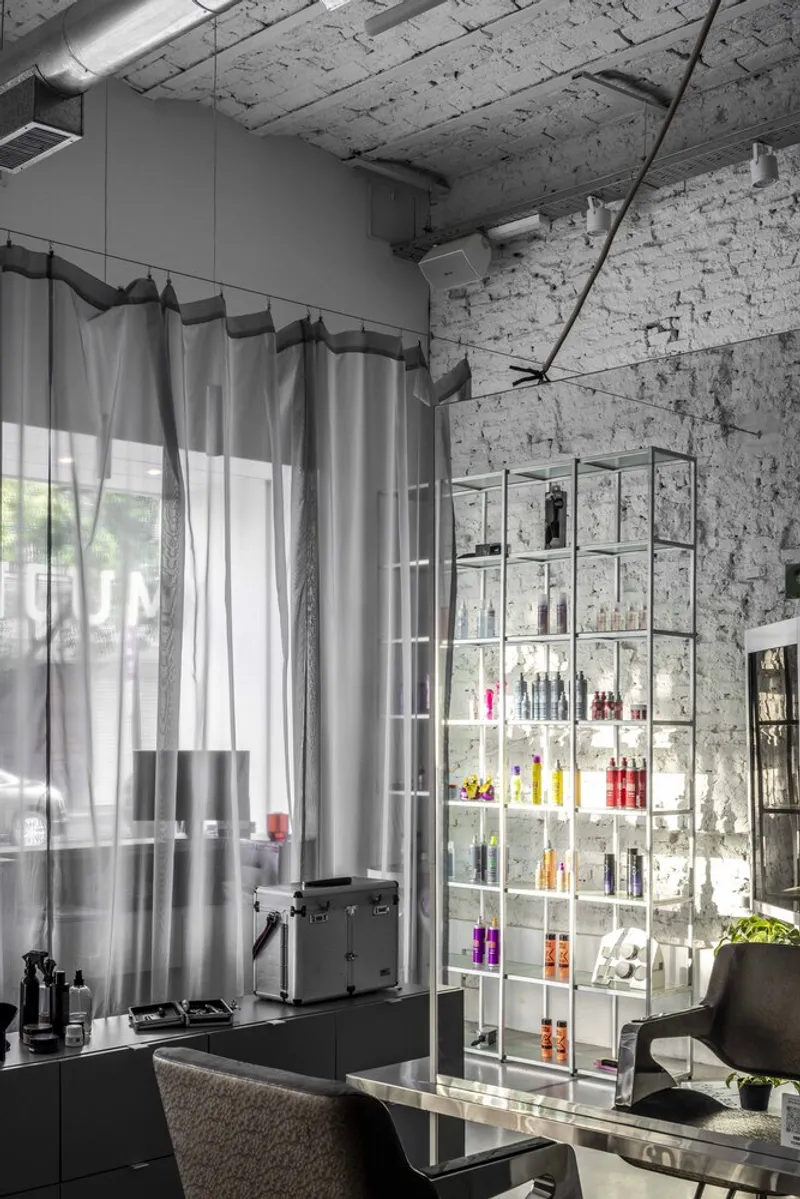 Glass product shelving unit against the white brick wall with grey curtains filtering light from the street