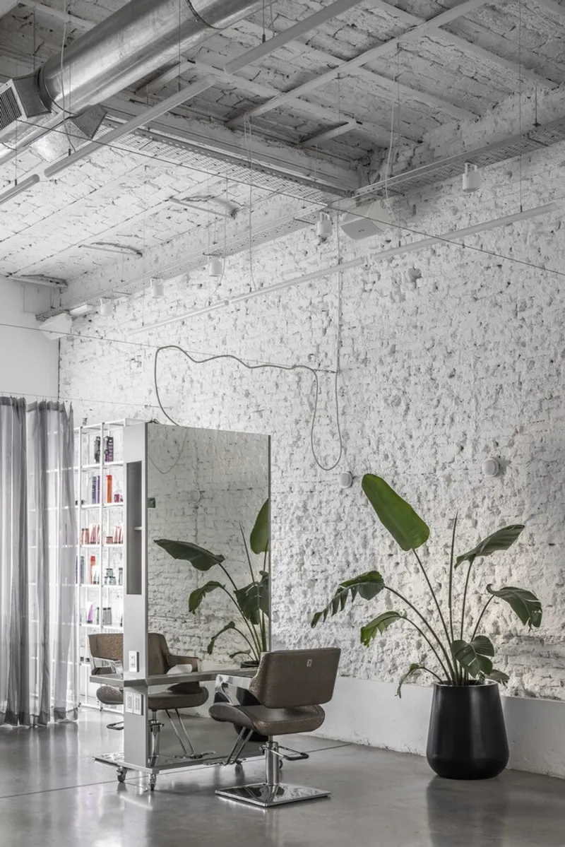 Styling station beside a black planter with bird-of-paradise beneath whitewashed brick walls and exposed ceiling ducts