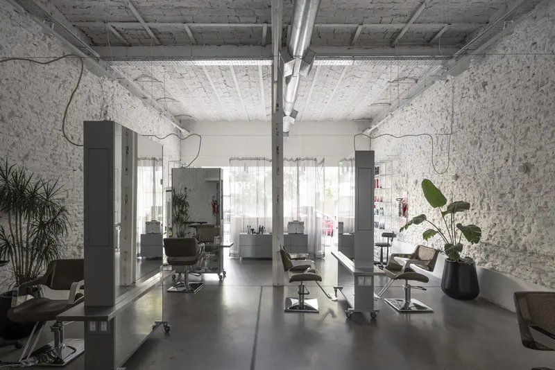Interior salon space with white painted brick walls, exposed ceiling ducts and potted plants between workstations
