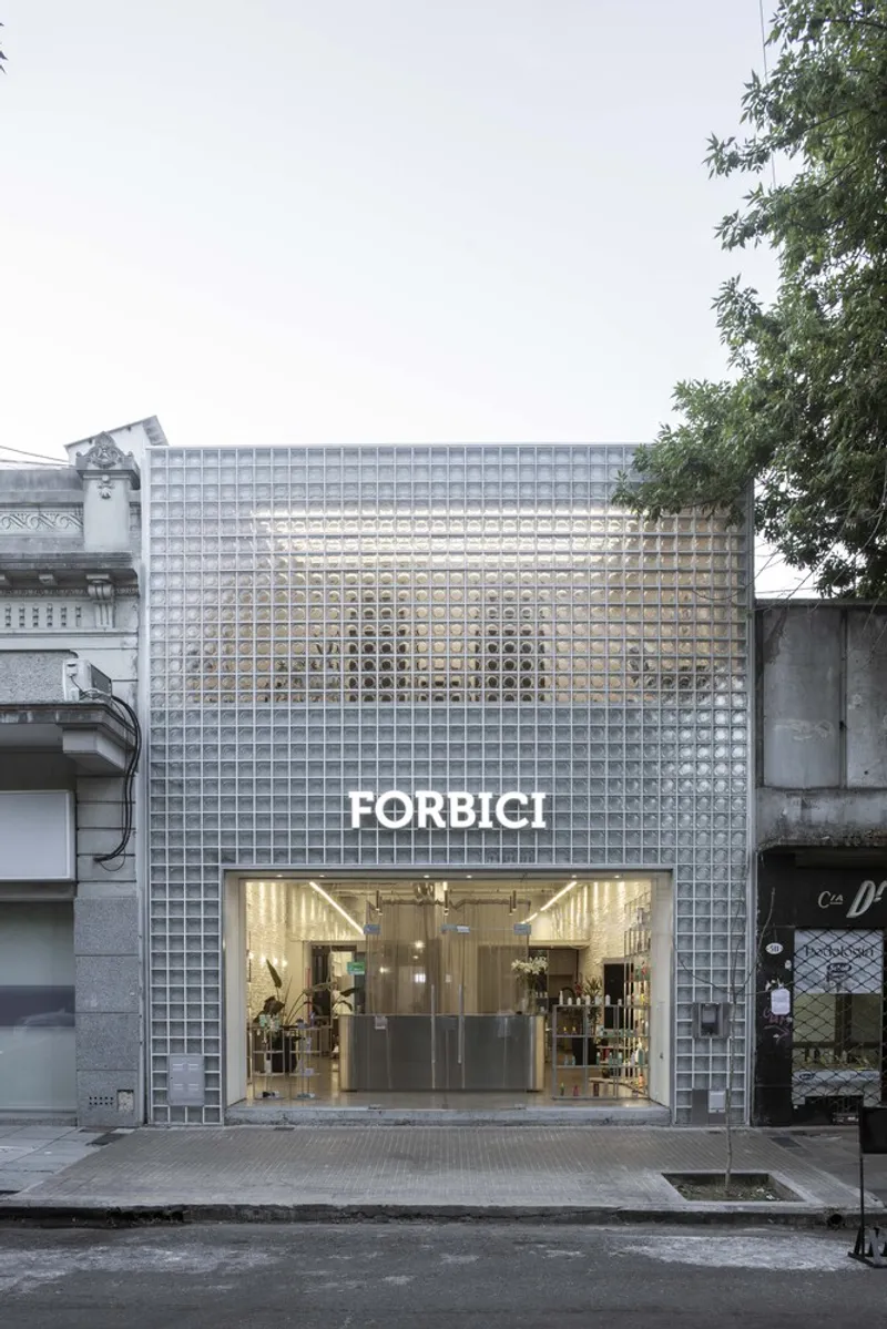 Street facade clad in translucent glass block with an overhanging tree beside the storefront entrance