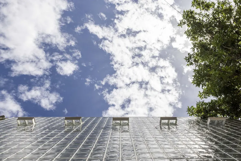 Upward view of the glass block facade with window openings against a cloudy sky