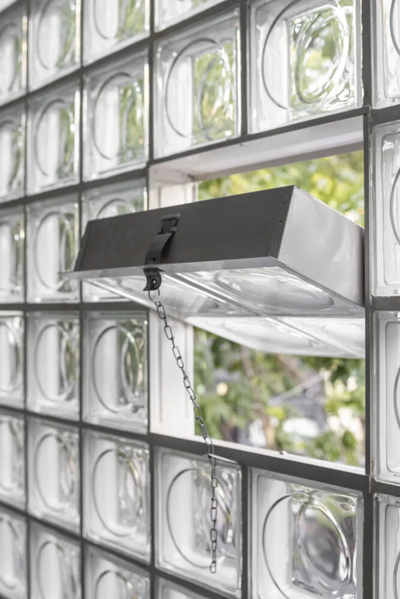 Detail of chain-operated awning window in glass block facade with greenery visible outside