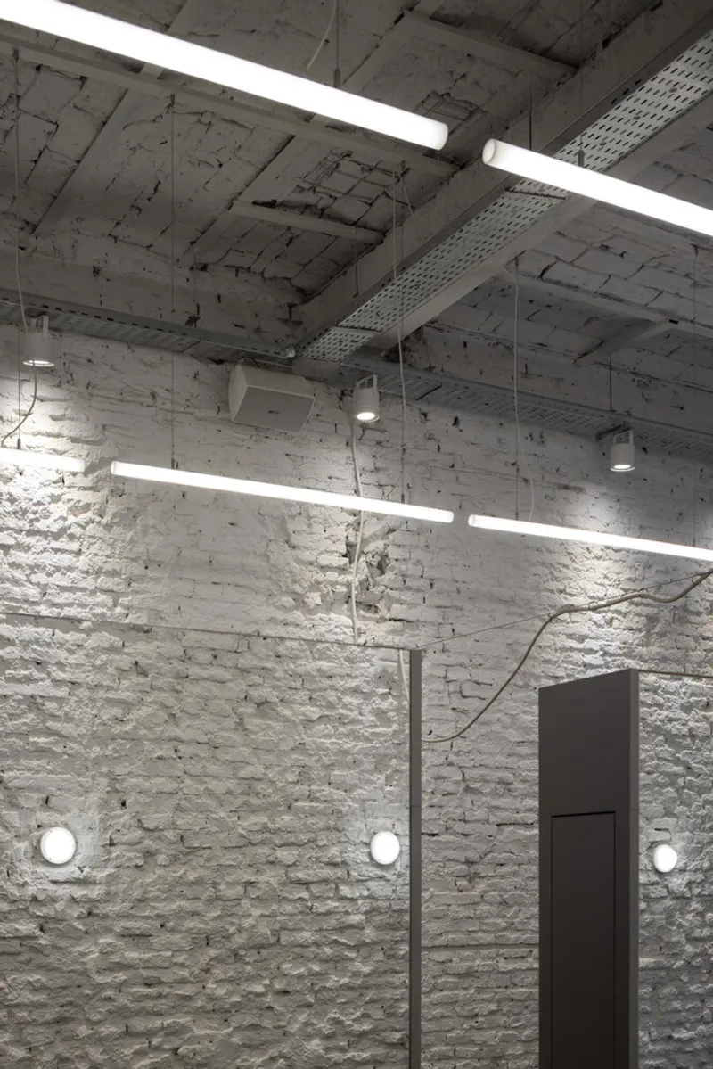 White painted brick wall with exposed concrete ceiling and suspended linear light fixtures