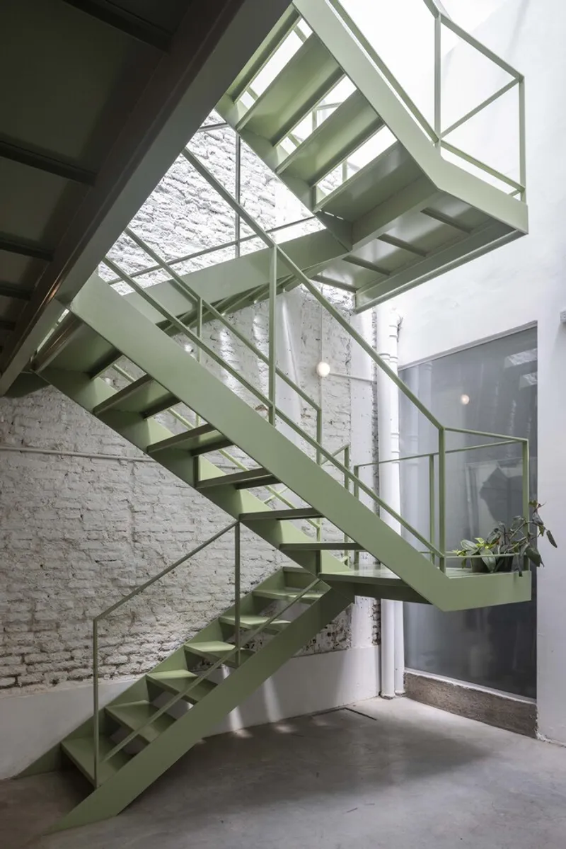 Pale green steel staircase with open risers against a white painted brick wall
