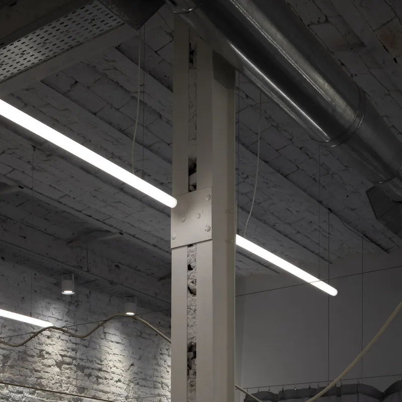 Steel column with exposed base and ductwork against painted brick under fluorescent tubes
