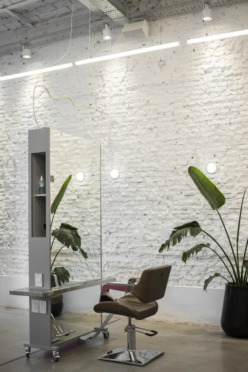 Single styling station against painted white brick wall with globe mirror lights and mobile cabinet