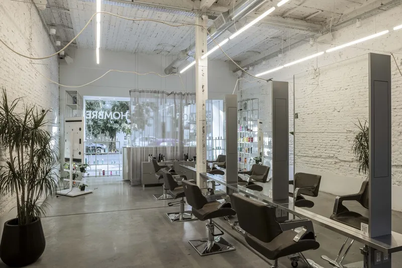 Row of salon chairs and mirrors along glass partitions with linear ceiling fixtures above