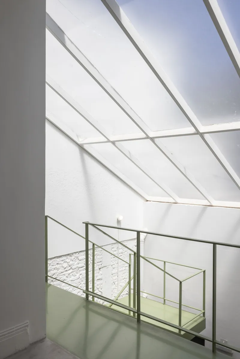 Stairwell with metal handrails beneath angled skylight casting diagonal shadows on white walls