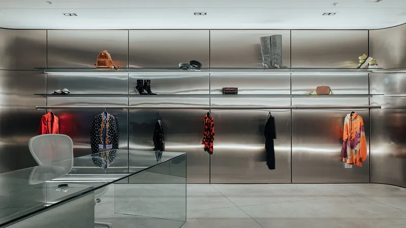 Backlit stainless steel display shelves with hanging garments and a translucent acrylic chair on polished concrete