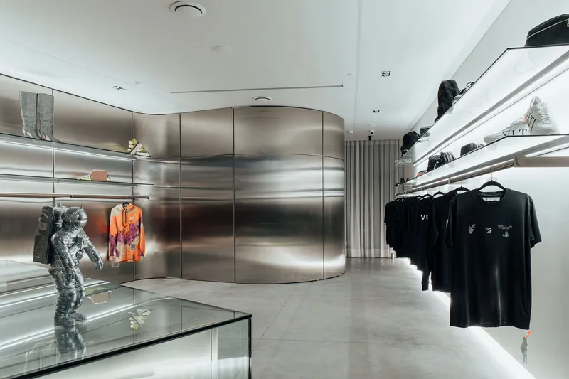 Curved stainless steel wall with integrated lighting bands and white display rails in a retail interior