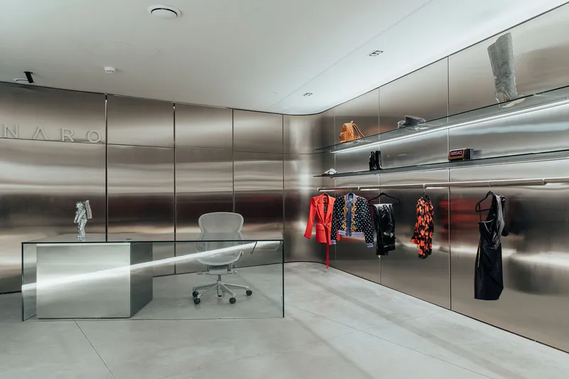Glass desk and white chair against reflective stainless steel panels with illuminated display niches above